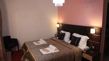 A hotel room with a bed, nightstands, a chair, and a chandelier.