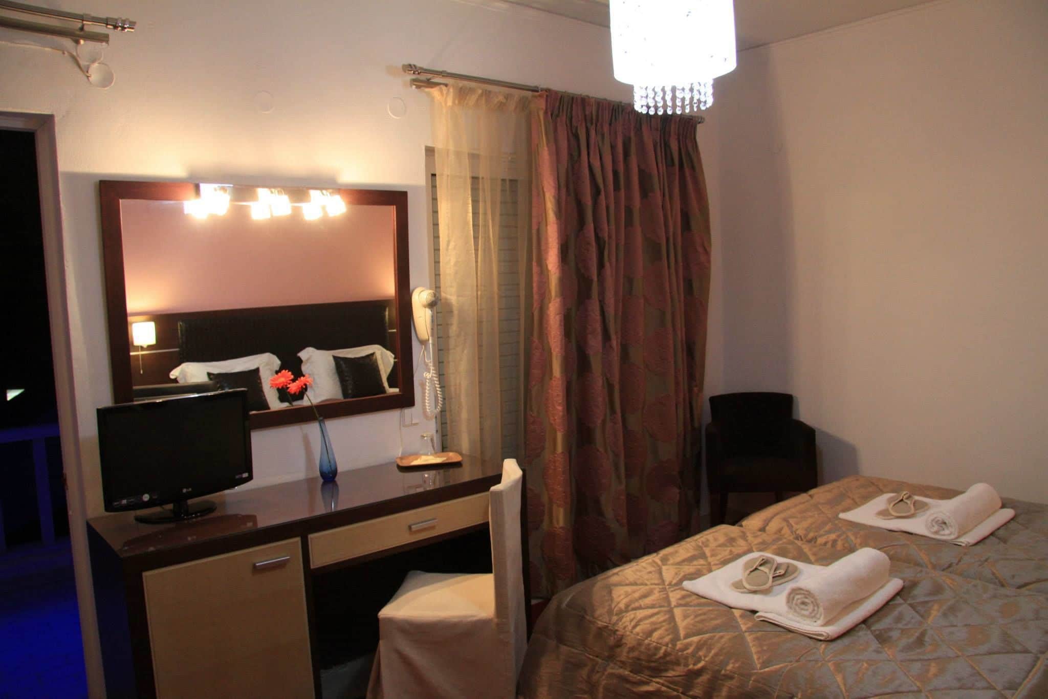 Habitación de hotel con cama, escritorio con computadora, espejo, teléfono y ventana con cortinas.
