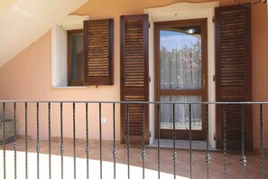 Ein Balkon mit schmiedeeisernem Geländer, eine Tür mit Holzhörnern und ein Fenster mit Blick auf Bäume und einen klaren Himmel.