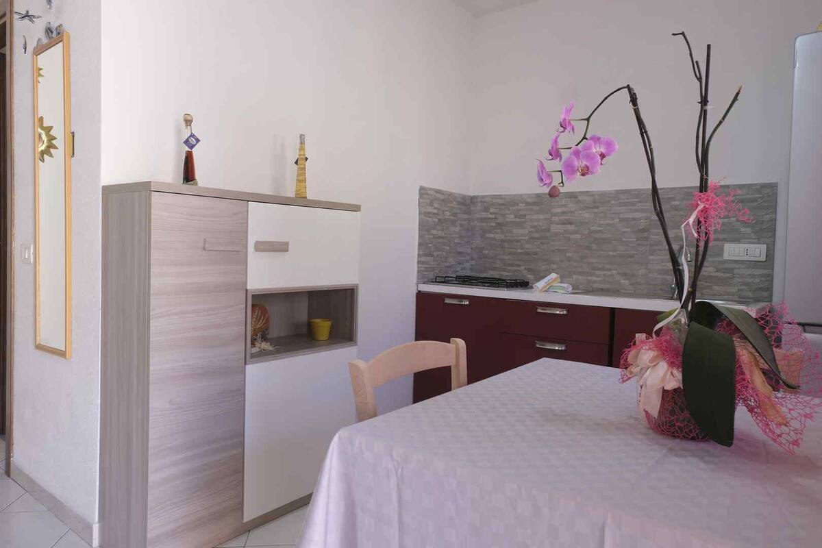 A compact kitchen with a white countertop, a built-in oven, and a vase with pink flowers.