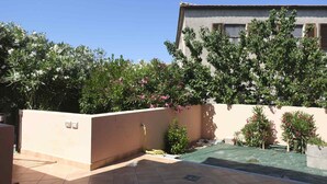 A courtyard with a tiled floor, a low wall, and a building in the background. - Aria di Vacanza - Zenzero (Olbia)