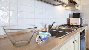 A kitchen with white tiles, stainless steel appliances, and a glass bowl on the counter. - Aria di Vacanza - Zenzero (Olbia)