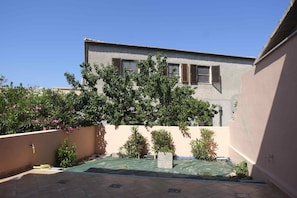 A courtyard with a building, a tree, and a hose. - Aria di Vacanza - Zenzero (Olbia)
