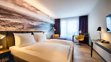 Ein Hotelzimmer mit einem großen Bett, einem Schreibtisch, einem Sessel und einem Bild an der Wand.