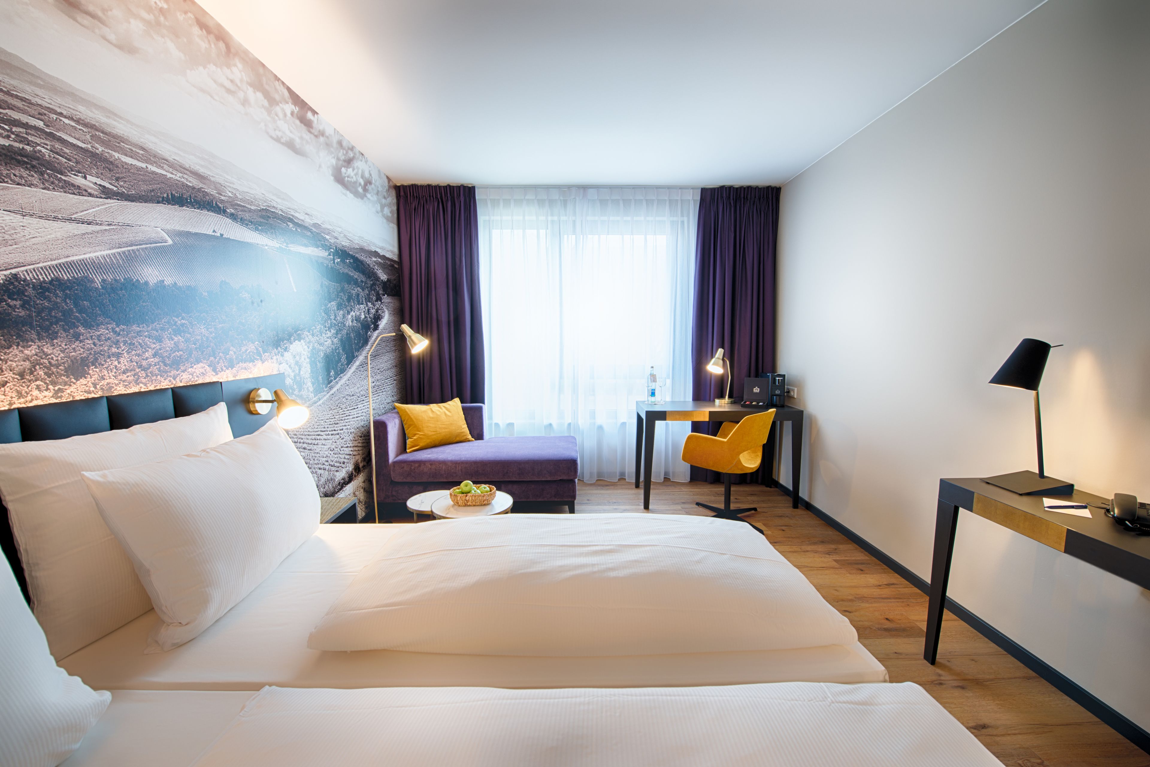 Ein Hotelzimmer mit einem großen Bett, einem Schreibtisch, einem Stuhl und Blick ins Freie.