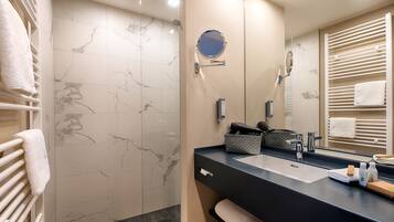 Un baño moderno con pared de ducha de mármol, un espejo grande, encimera negra y un perchero para toallas.
