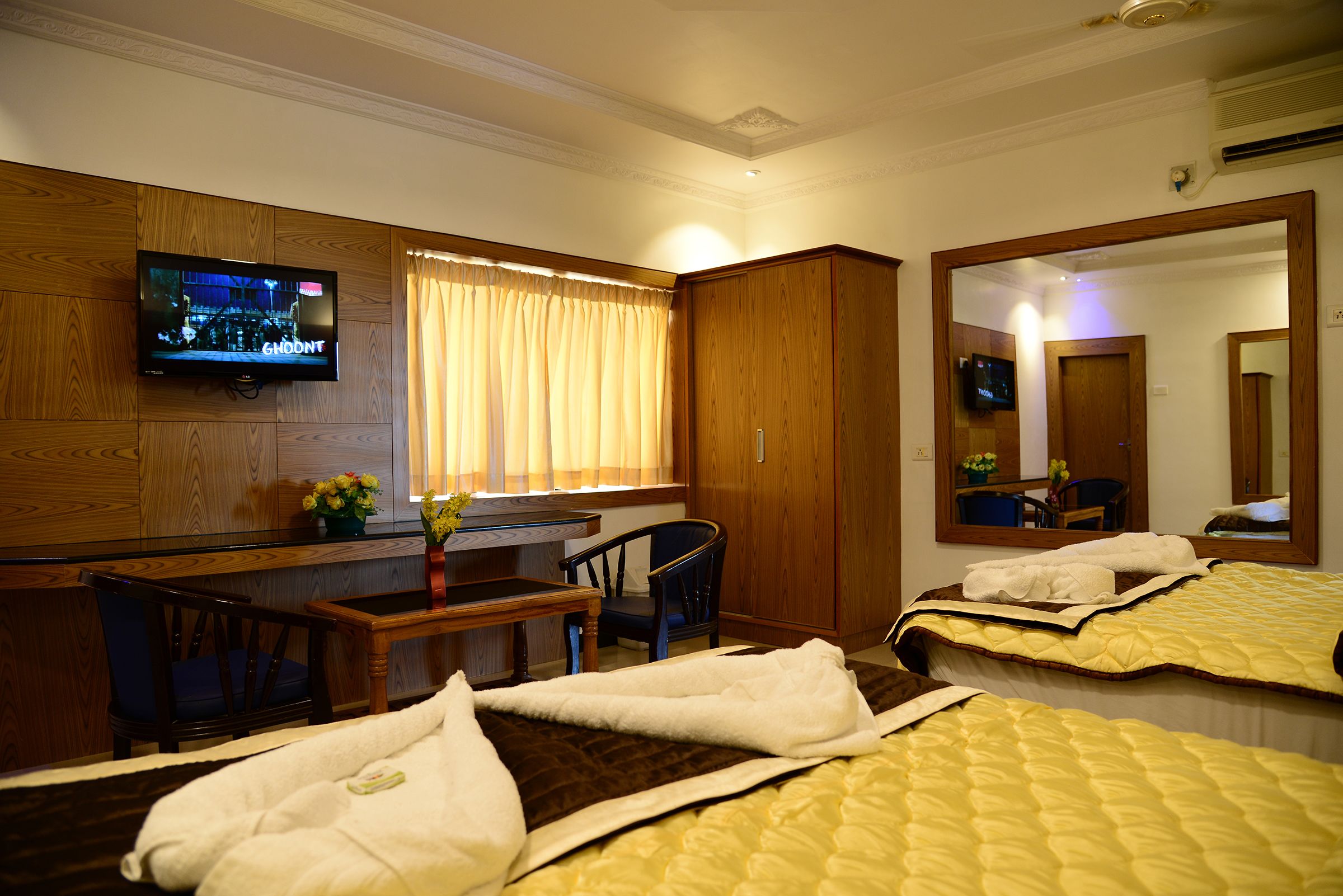 Une chambre d’hôtel équipée d’un téléviseur fixé au mur, d’un bureau avec une chaise, d’un lit avec une couvre-lit matelassé et d’un grand miroir.