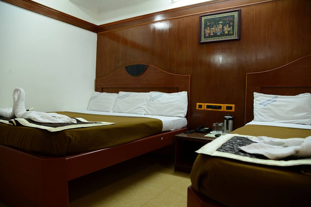 Ein Hotelzimmer mit zwei Betten, Holz-Kopfteilen, weißen Bettwäsche, einem gerahmten Bild an der Wand und einem kleinen Tisch mit Telefon und Flasche.