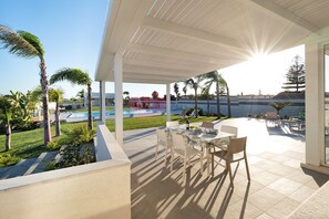 Relax outdoors with a dining table for two, overlooking a serene pool and lush lawn.