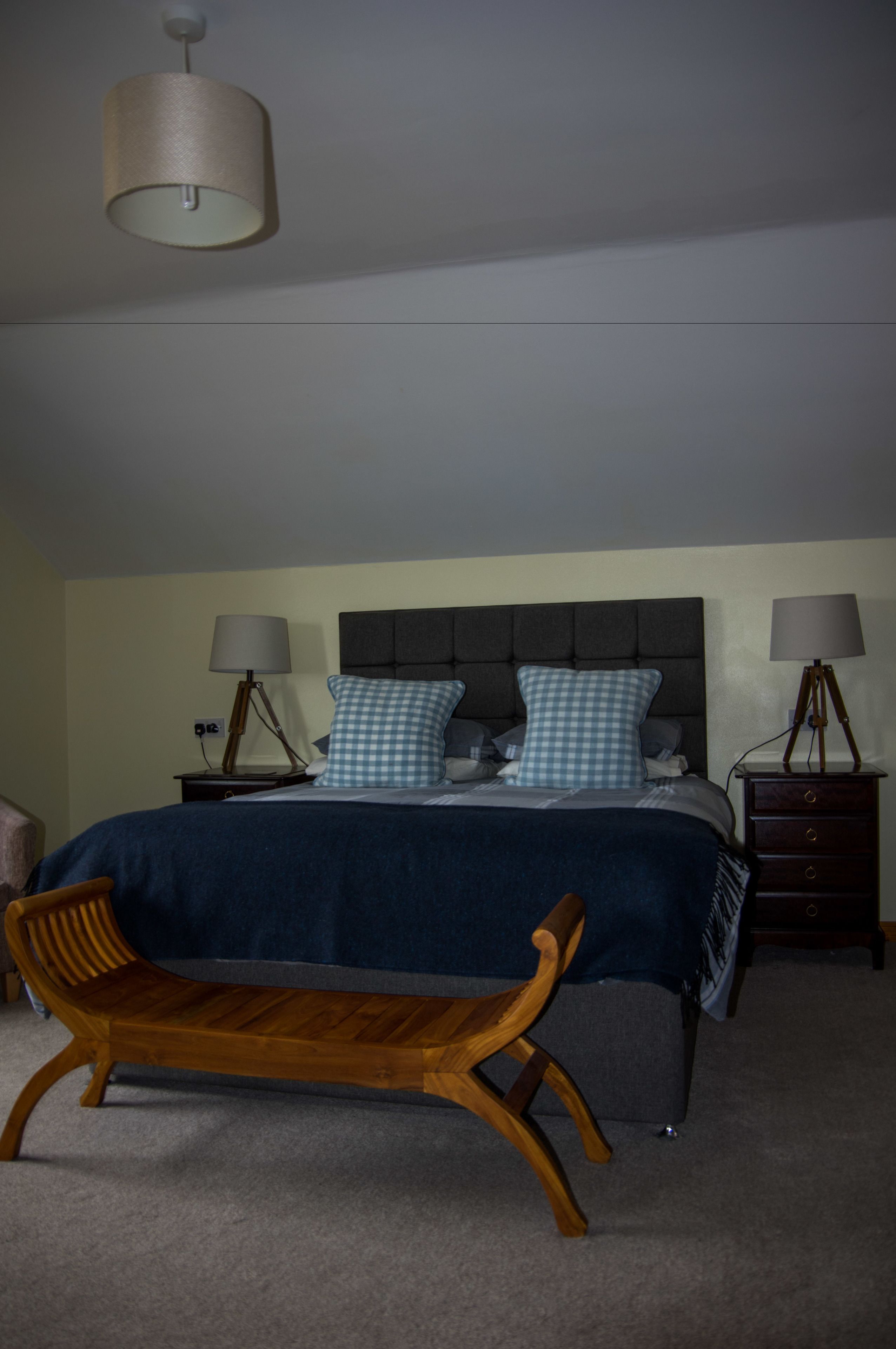 Une chambre à coucher avec un lit, deux tables de chevet avec des lampes, un banc et un luminaire suspendu.