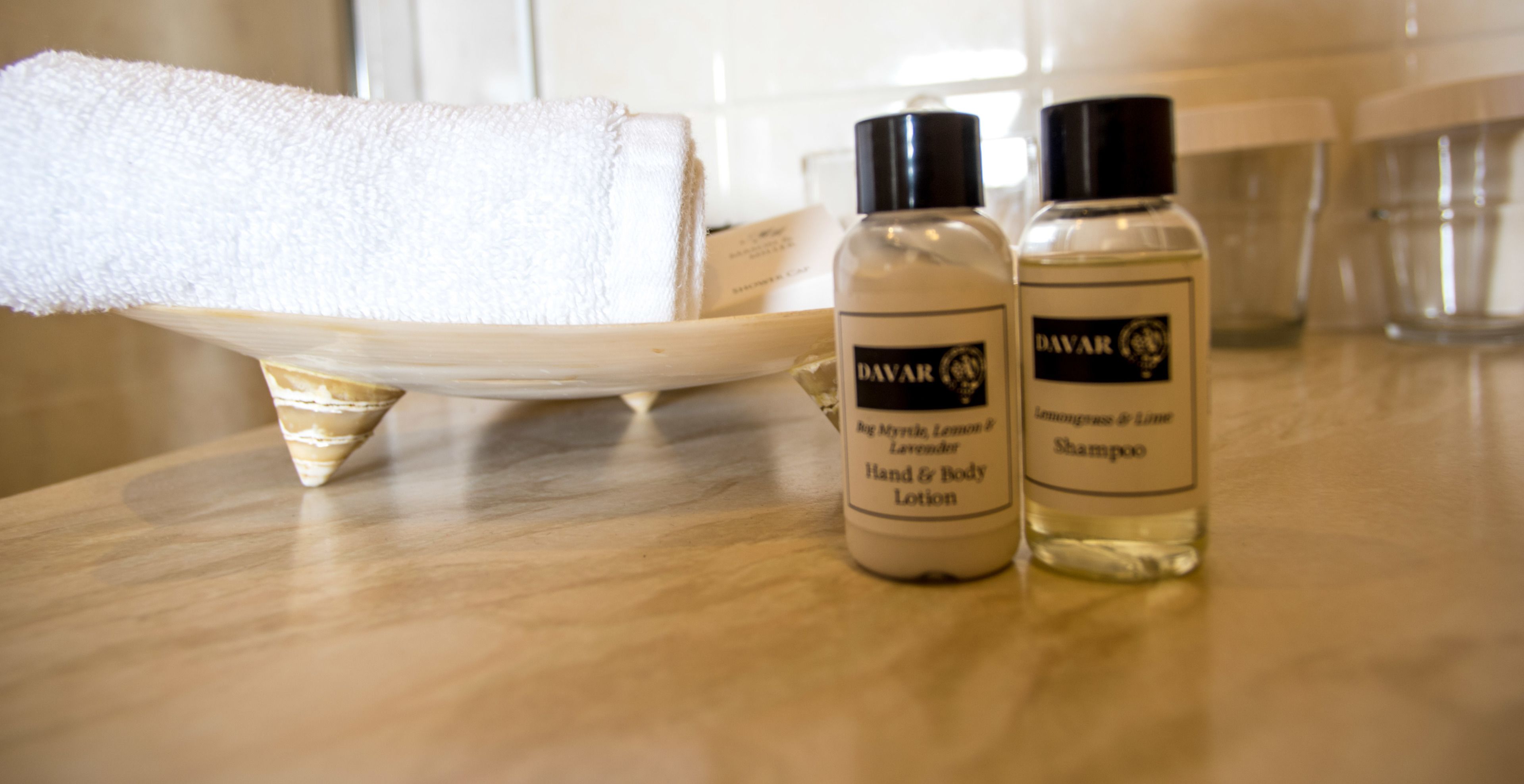 A bathroom counter with a white towel, a bottle of hand and body lotion, and a bottle of shampoo.