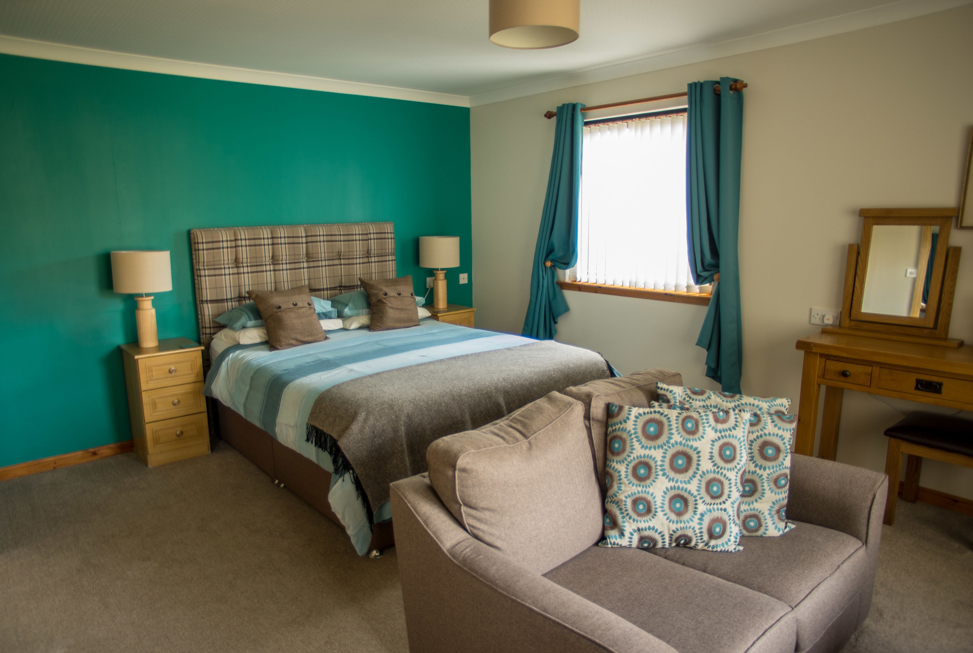 A bedroom with a bed, a dresser, a chair, and a window with curtains.