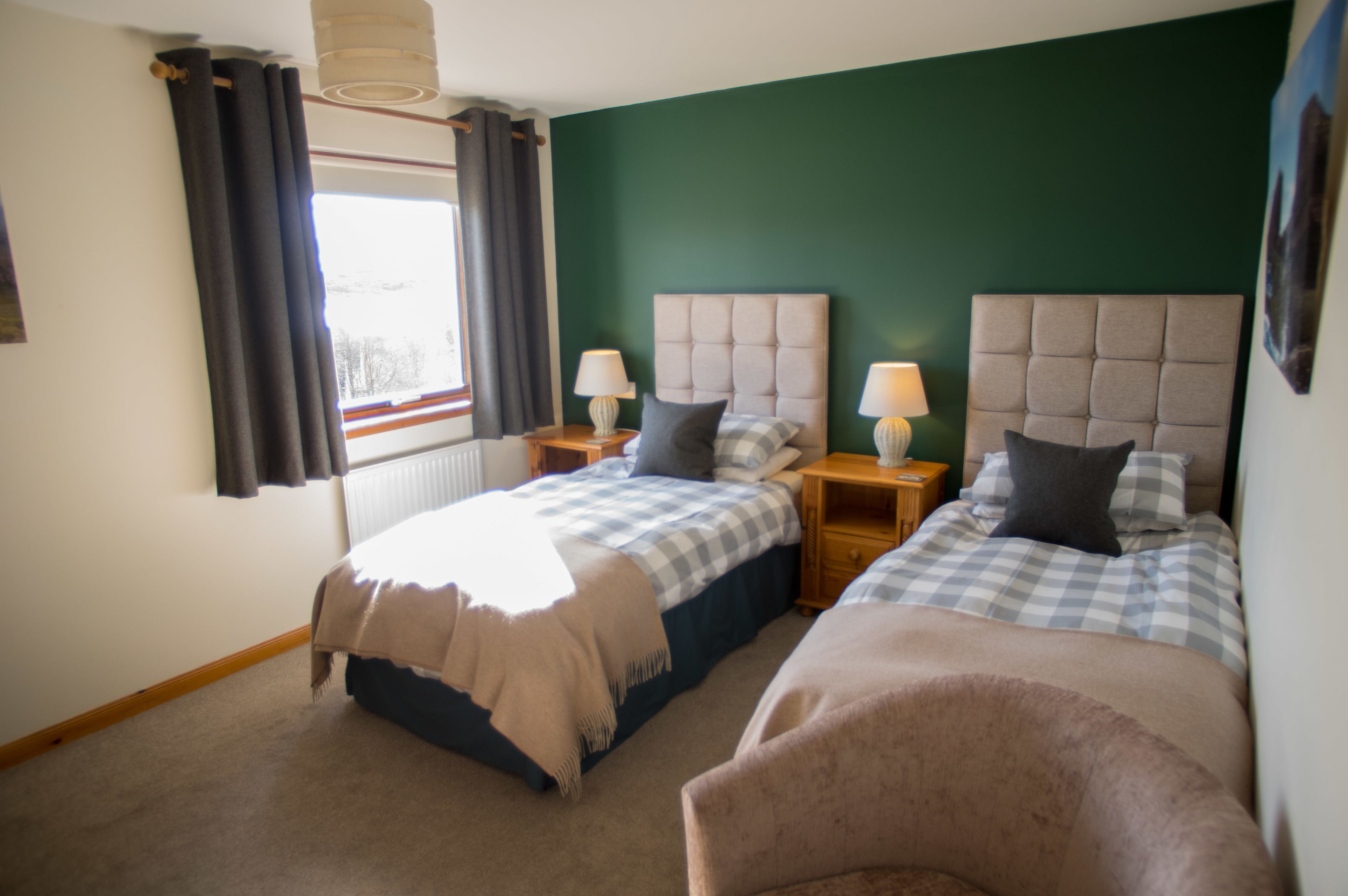A hotel room with two beds, a window with curtains, bedside lamps, and a green accent wall.