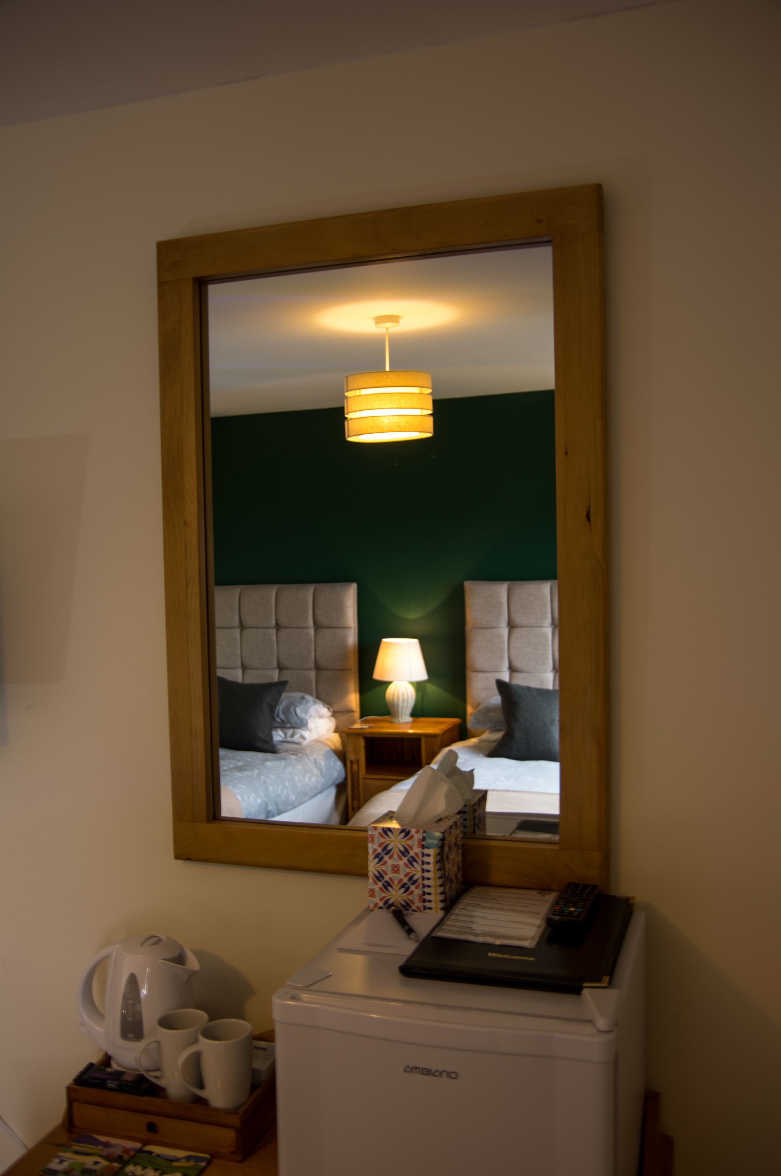 A hotel room with a bed, bedside table, lamp, and a mirror reflecting the room.
