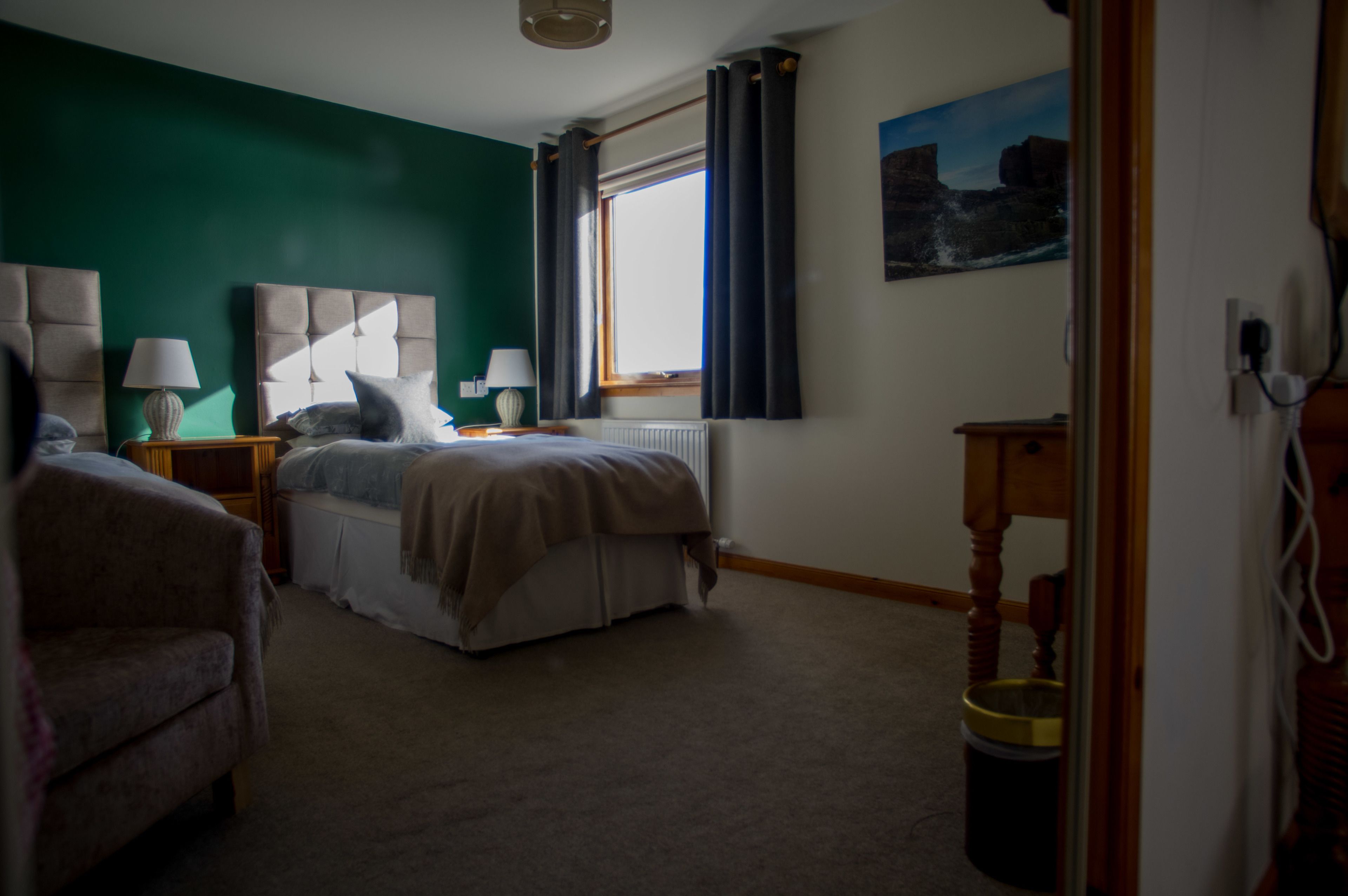 Une chambre à coucher avec un lit, des tables de chevet, une lampe, un radiateur, une fenêtre avec des rideaux et un tableau au mur.