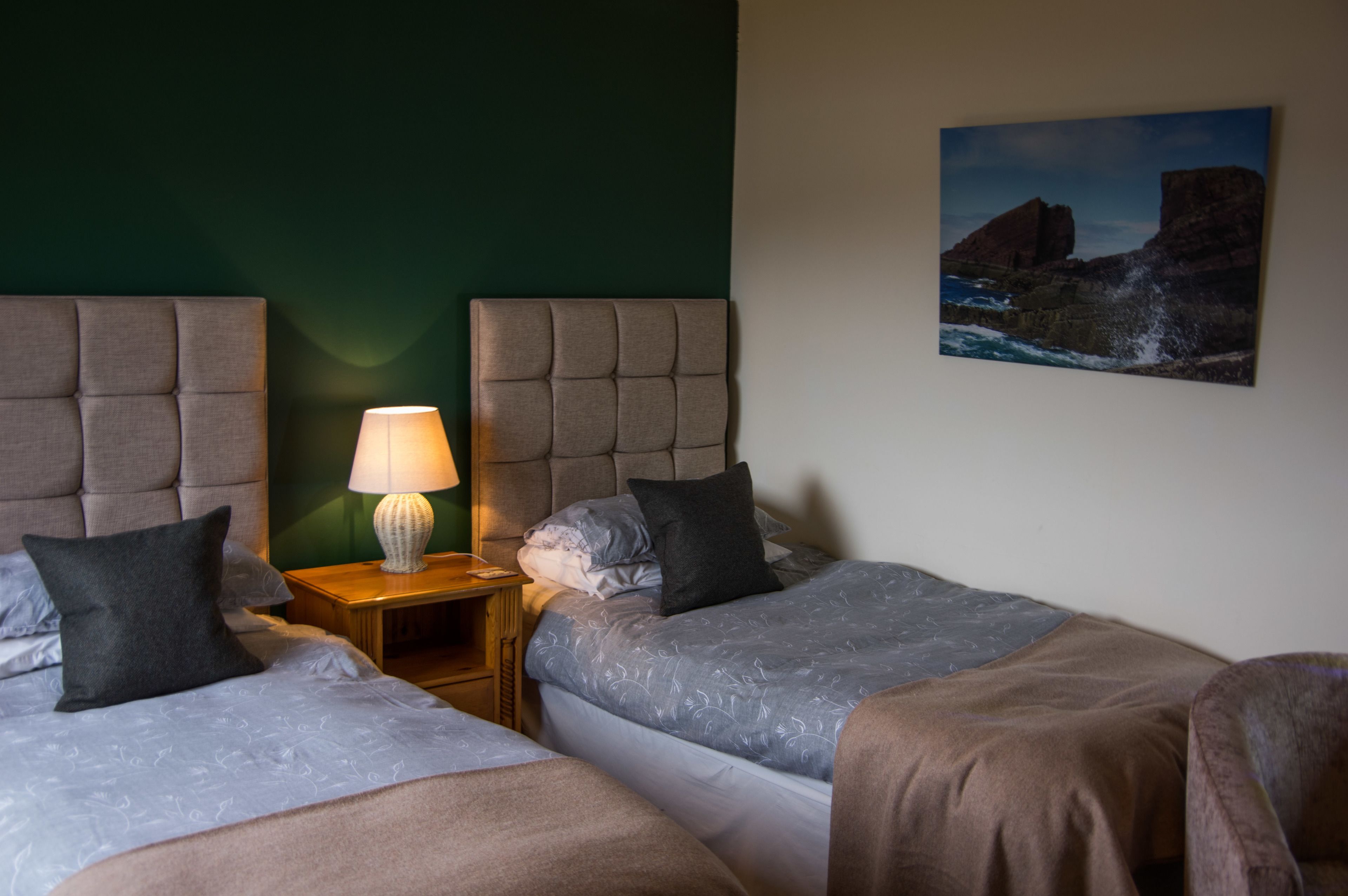 Una habitación de hotel con dos camas, una mesita de noche con lámpara y un cuadro en la pared.