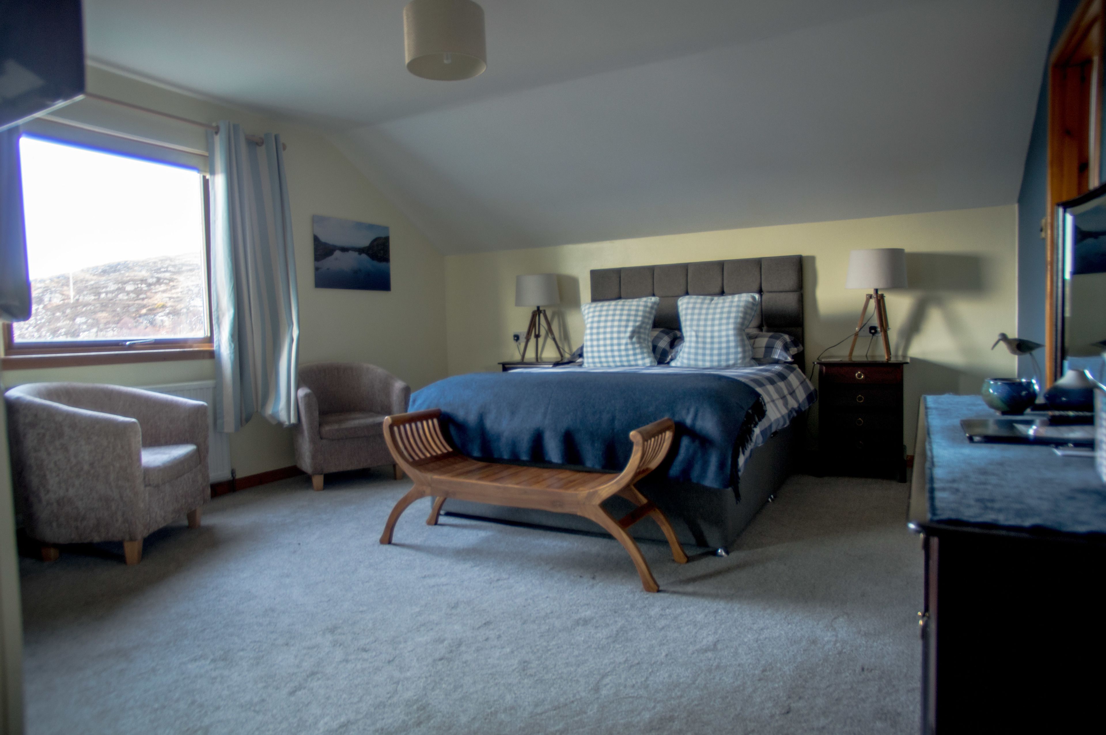 A bedroom with a bed, a bench, a chair, a nightstand, and a lamp.