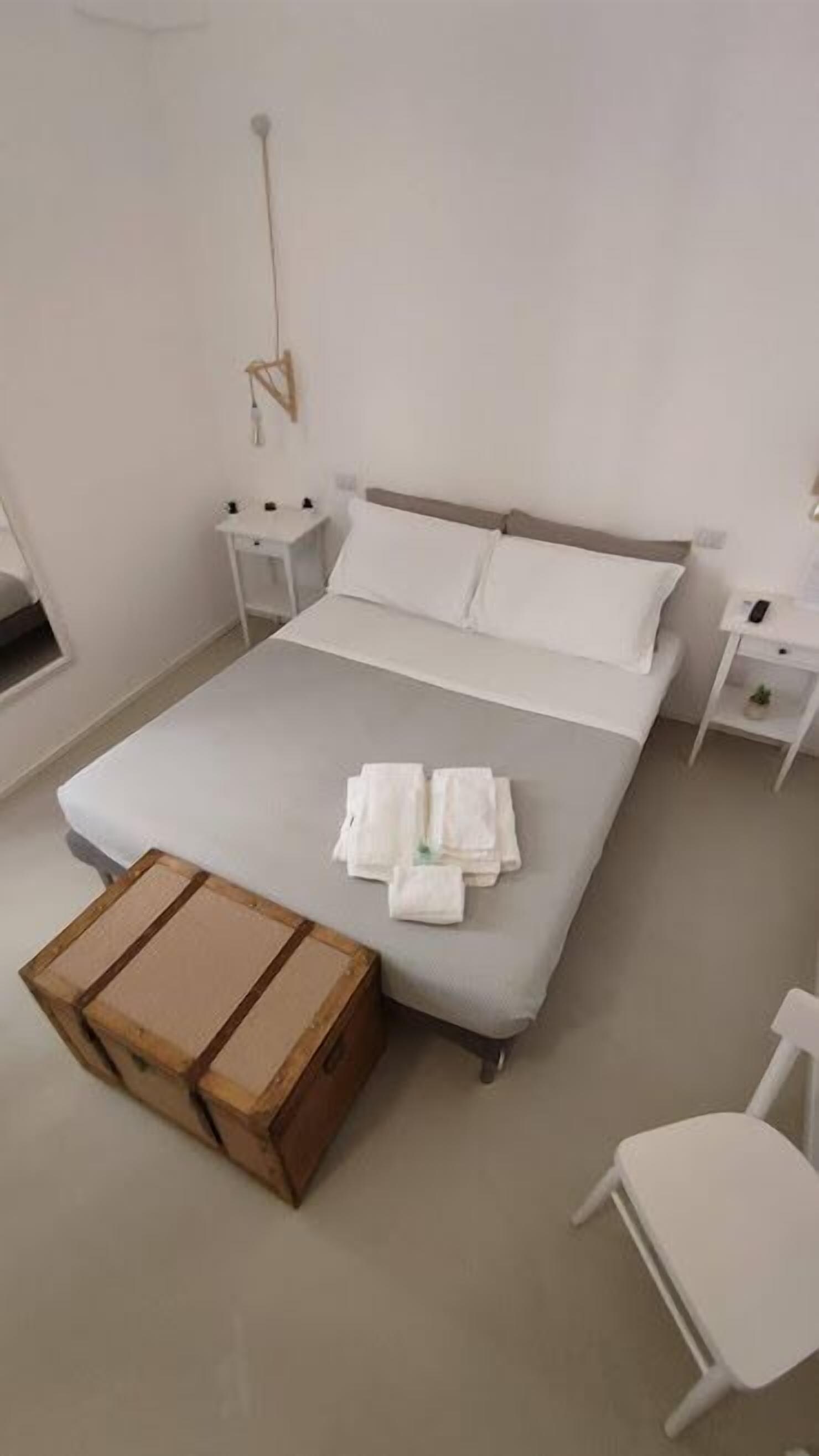 Ein ordentlich eingerichtetes Schlafzimmer mit Bett, Nachttischen, einem Koffer und einem Sessel.