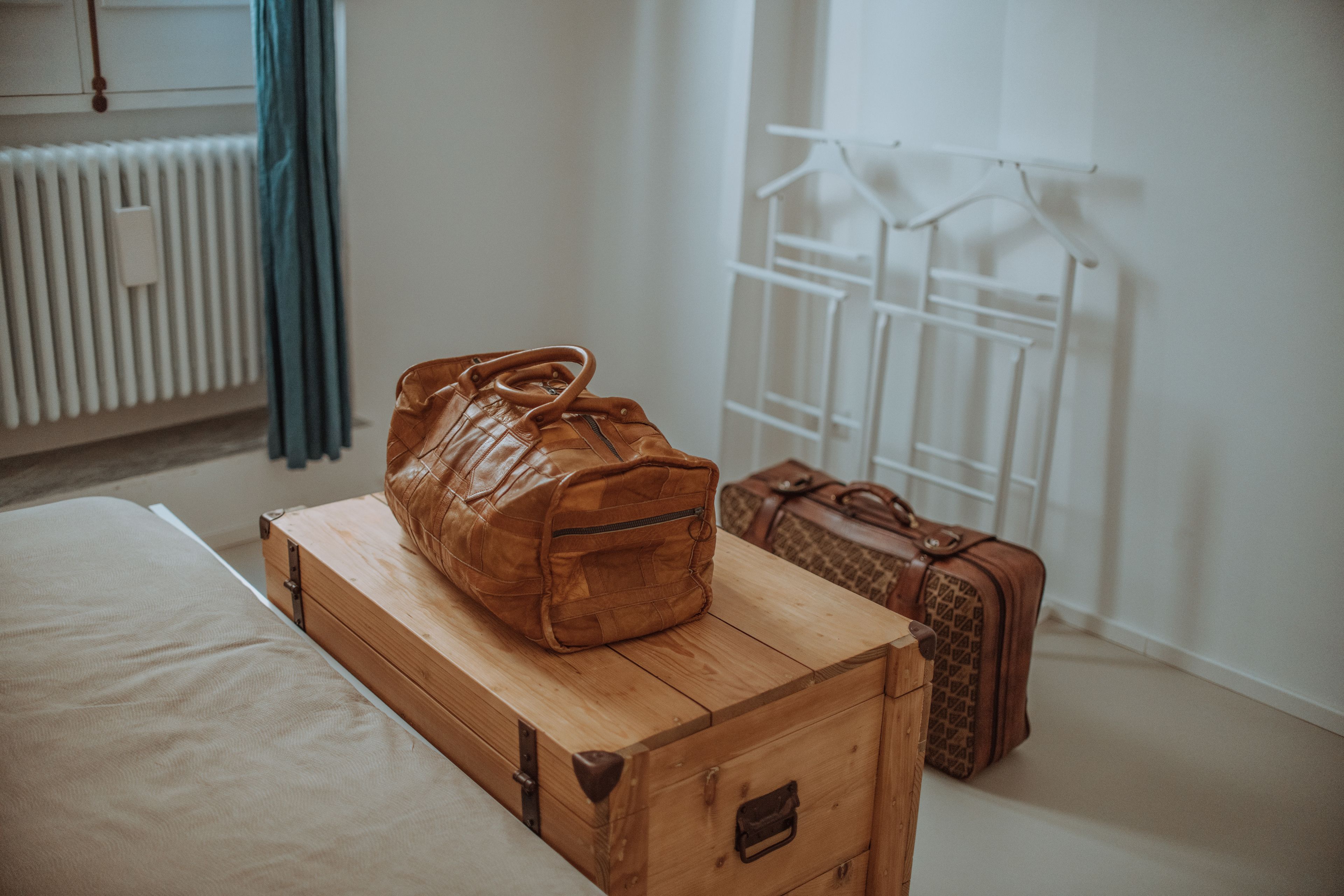 Un baúl de madera con una bolsa grande marrón y dos maletas pequeñas en una habitación de hotel.
