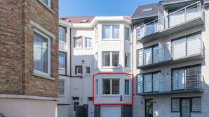 A multi-story residential building with a white facade, a garage door, and a balcony on the upper floor. - Clos 1 (De Panne)