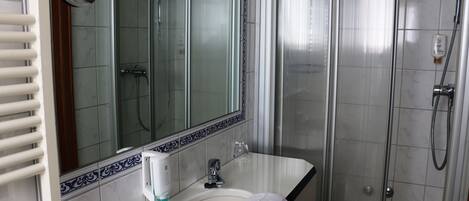 Un baño con lavamanos blanco, un espejo, una toalla y cabina de ducha.