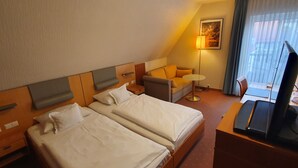 A hotel room with two beds, a sofa, a desk with a computer, a lamp, and a painting on the wall. - Baumhove Hotel Restaurant Am Markt (Werne)