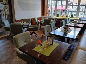 A restaurant interior with multiple tables and chairs, a menu on the table, and a view of the street through large windows. - Baumhove Hotel Restaurant Am Markt (Werne)