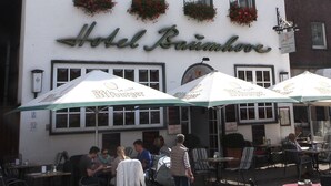 A building with a sign reading "Hotel Baumberg" and outdoor seating with umbrellas. - Baumhove Hotel Restaurant Am Markt (Werne)