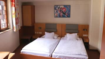 Habitación de hotel con dos camas individuales, un escritorio, una silla, un armario y un cuadro en la pared.