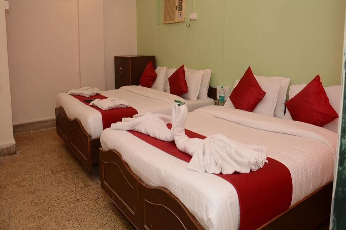 A hotel room with two beds, each with white linens and red pillows, and a wooden headboard.