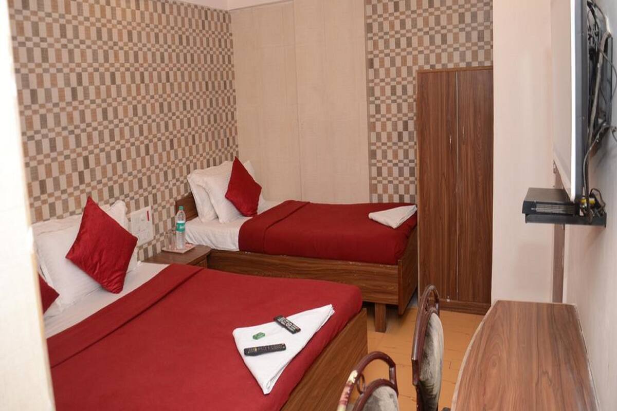 A hotel room with two beds, each with red bedding and pillows, a wooden wardrobe, and a television mounted on the wall.