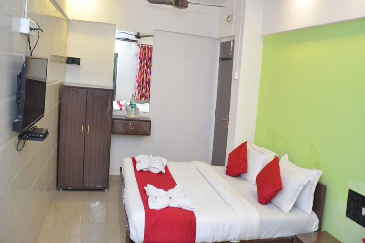 A hotel room with a bed, a TV, a wardrobe, and a green accent wall.