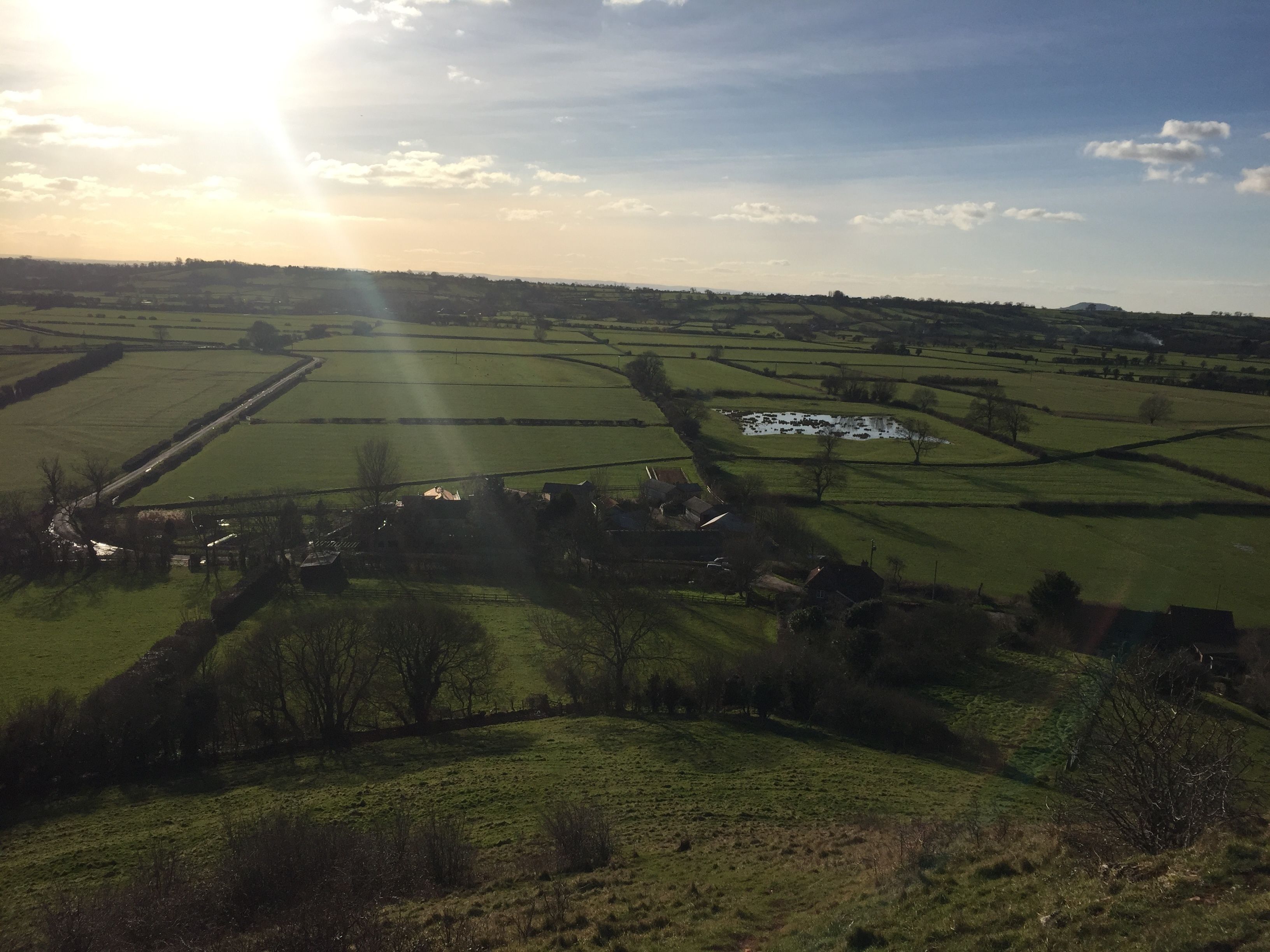 A rural landscape with fields, a small village, and a distant hill.