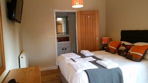 A hotel room with a bed, a wooden wardrobe, a mirror, a bedside table, and a lamp. - Tor Farm Lodge (Cheddar)