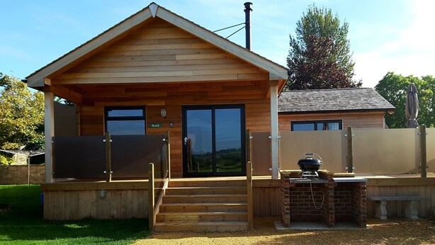 A wooden cabin with a covered porch, a grill, and a nameplate reading "Bluebell". - Tor Farm Lodge (Cheddar)
