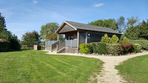 A building with a sloped roof, a covered entrance, and a paved pathway leading to it. - Tor Farm Lodge (Cheddar)