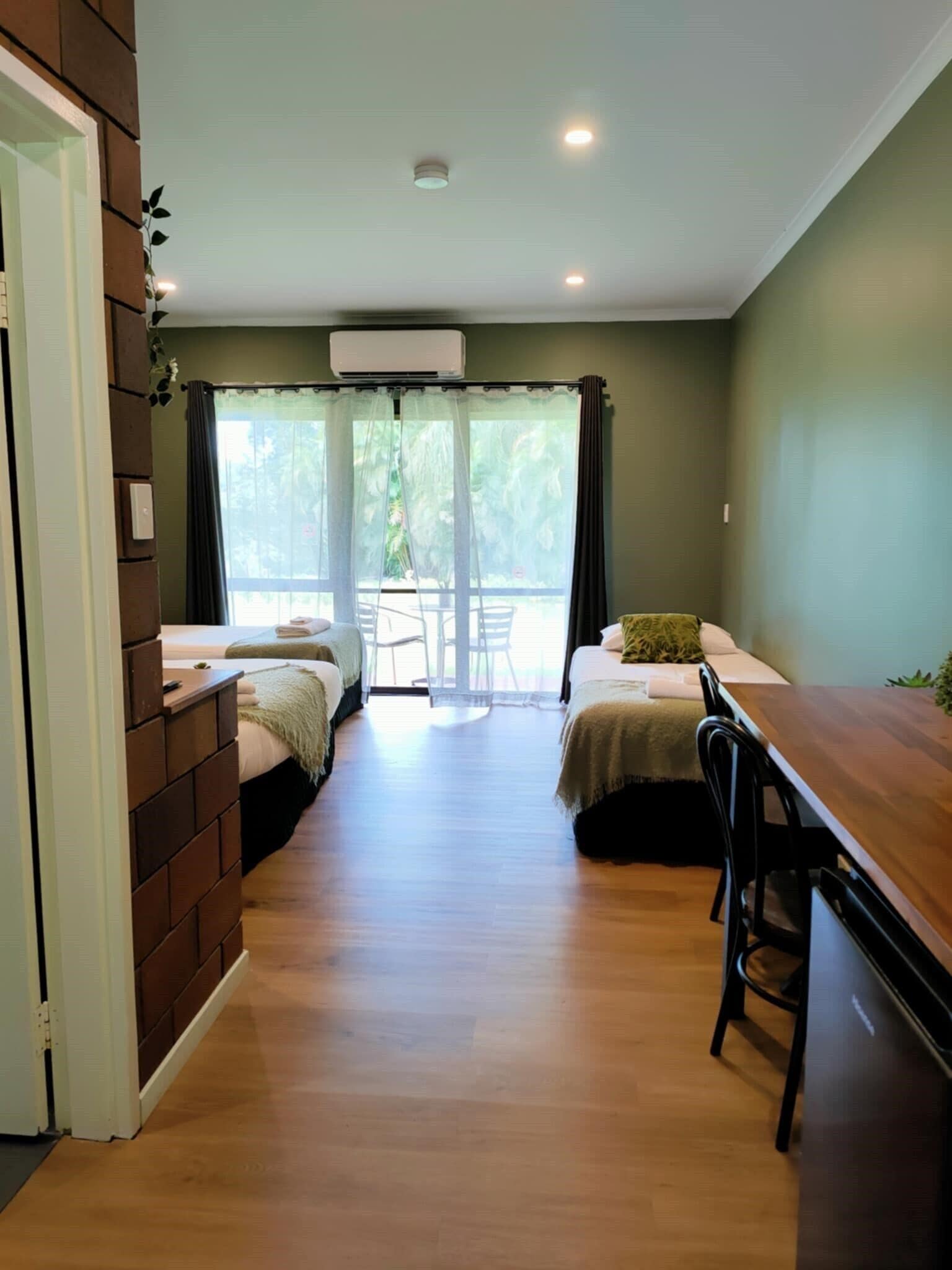 Habitación con dos camas, una mesa de madera y vistas al verdor exterior.
