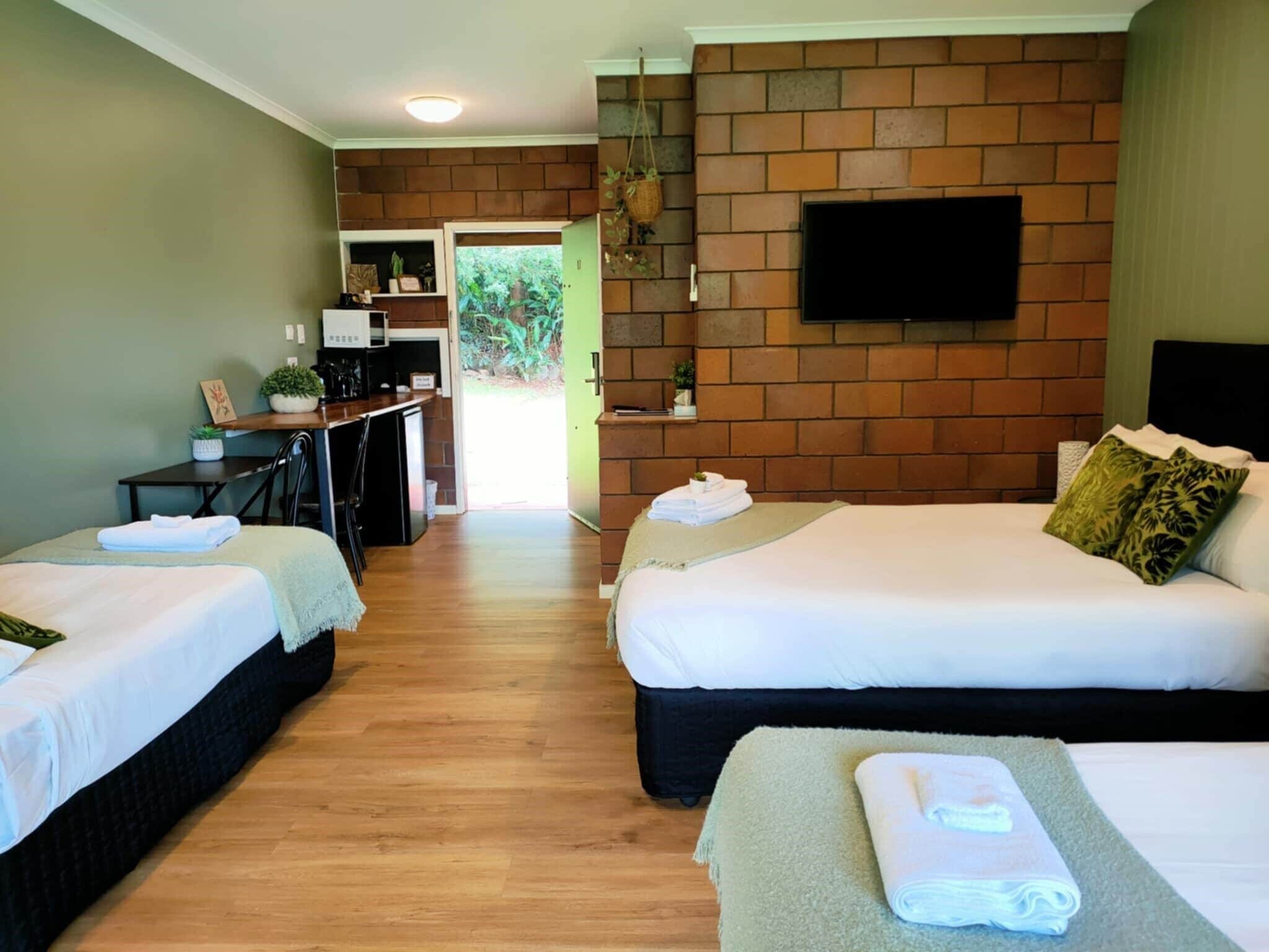 Une chambre d’hôtel avec deux lits, une kitchenette, un téléviseur fixé au mur en briques et une vue sur l’extérieur.