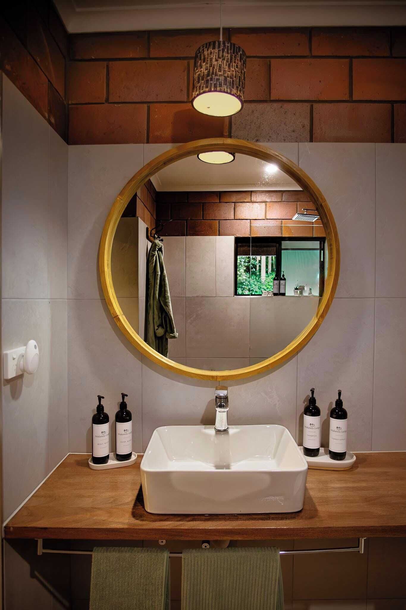Un baño con un lavabo rectangular, un espejo redondo y dos botellas de champú.