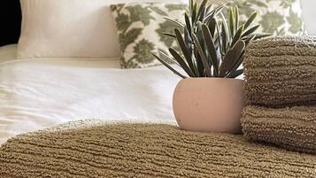 A neatly made bed with white and patterned pillows, a small potted plant, and a folded textured blanket.