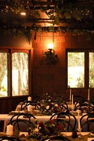Comedor con paredes de ladrillo, plantas colgantes y una mesa para dos con velas y un centro de mesa floral.