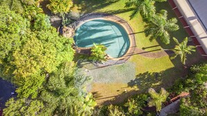 An aerial view of a residential area with a swimming pool surrounded by lush greenery and a house with a sloped roof.