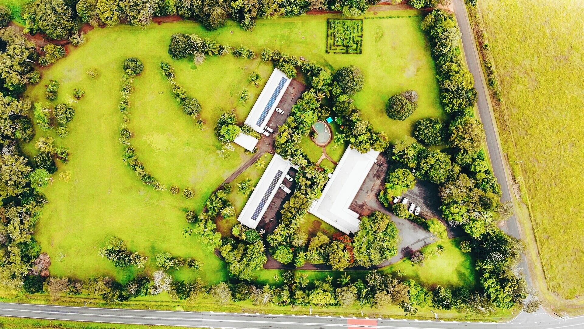 Vista aérea de una propiedad con un amplio campo verde, dos edificios y una carretera.