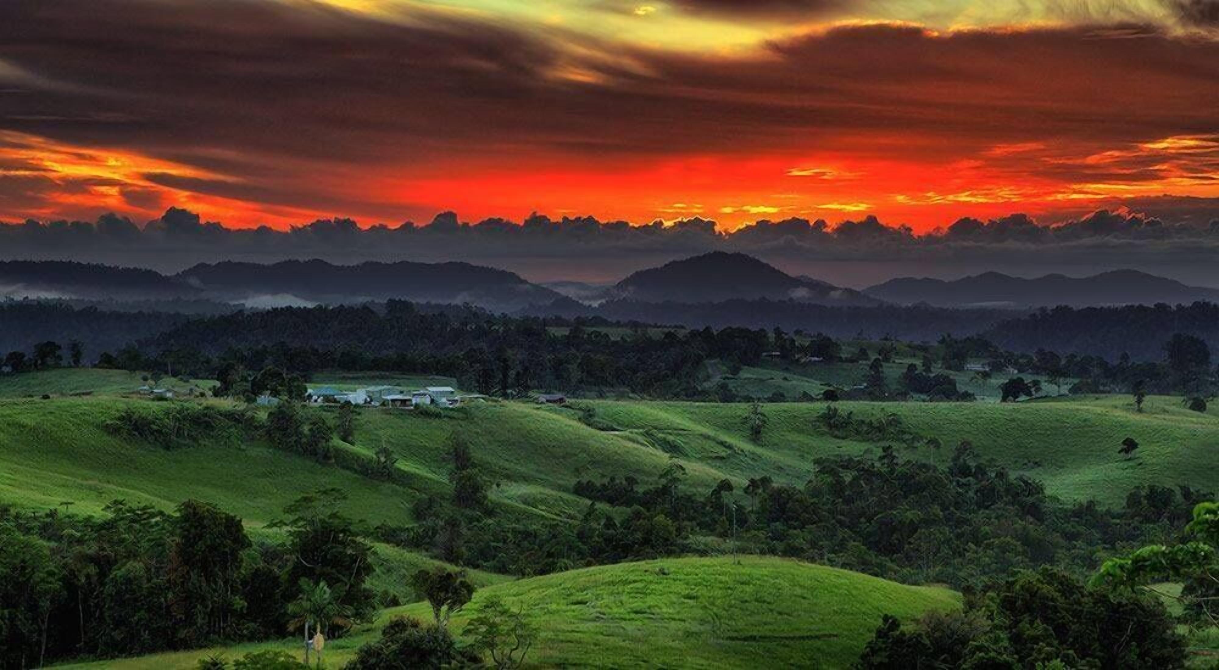 A landscape with rolling hills, a small building, and a sunset.