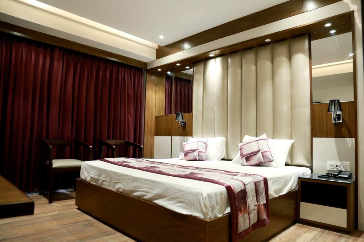 Quarto de hotel com cama grande, escrivaninha, cadeira, espelho e janela com cortinas.