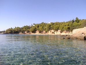Paisaje costero con agua cristalina, una playa de arena y una ladera boscosa.