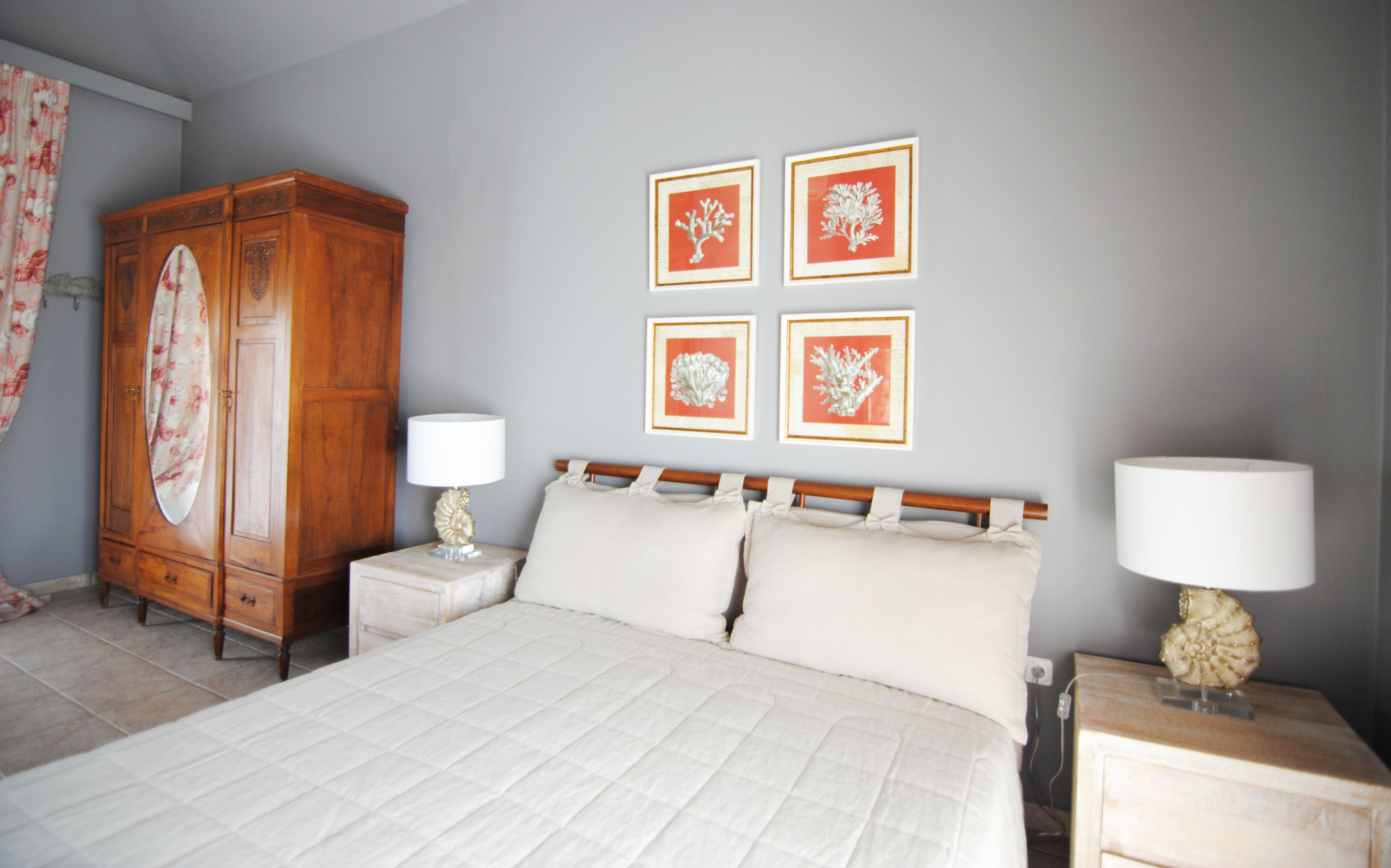 A bedroom with a bed, two bedside tables, a wooden wardrobe, and four framed coral artwork on the wall.