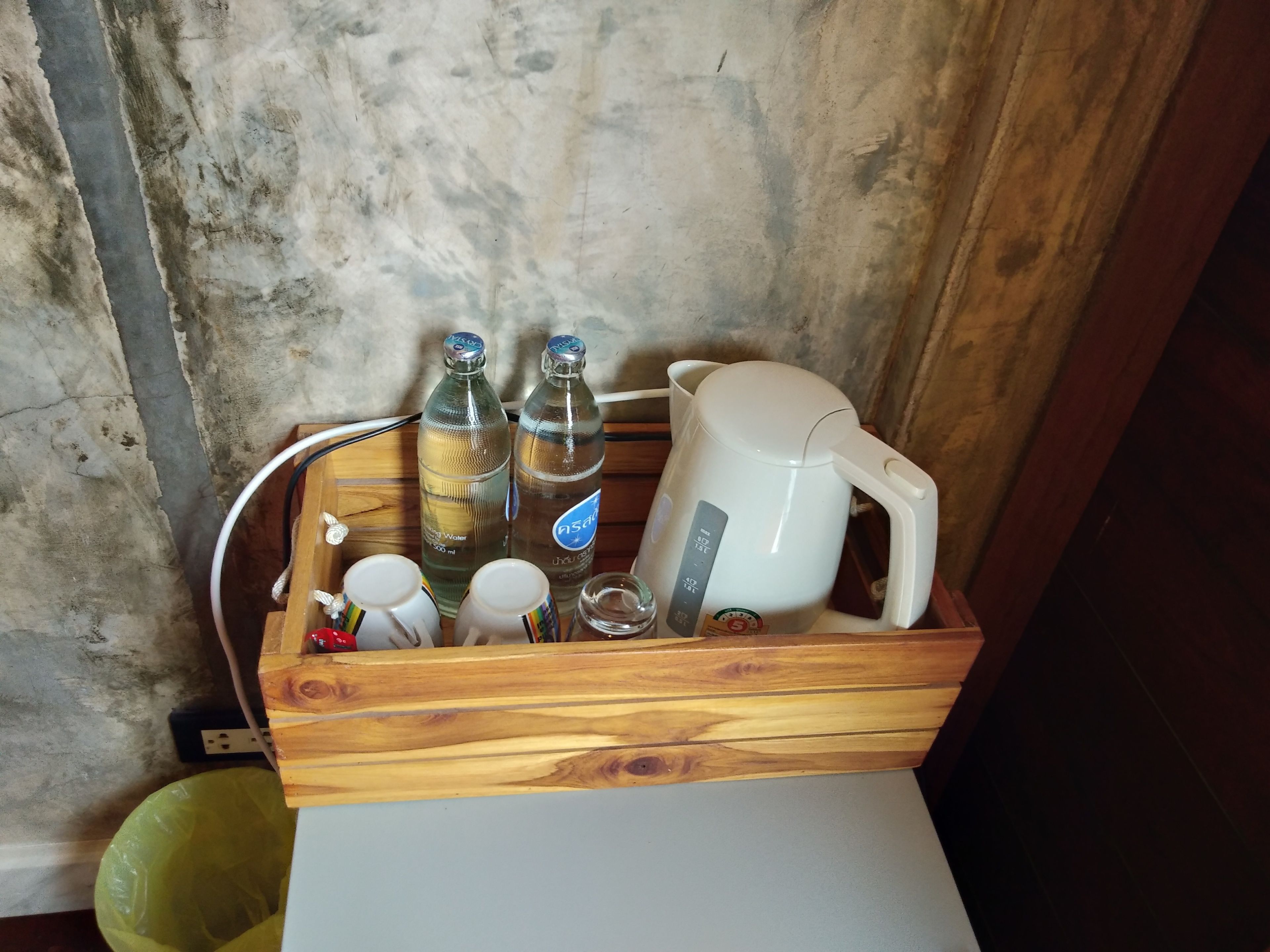 Un plateau en bois contenant une bouilloire électrique blanche, deux bouteilles en verre, un verre et un sac en plastique.