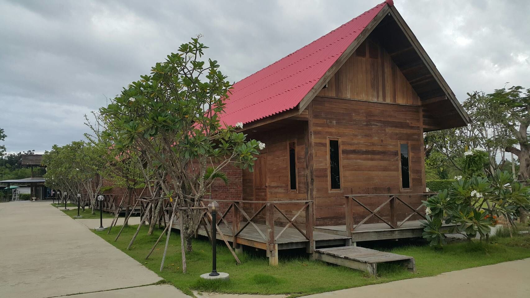 A wooden cabin with a red roof, surrounded by a wooden deck and small trees.
