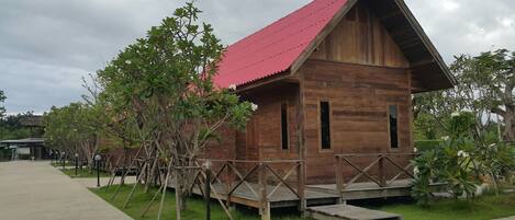 A wooden cabin with a red roof, surrounded by a wooden deck and small trees.